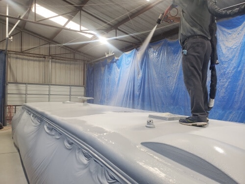 An employee treating an rv roof by spraying the "Flexarmor" sealant that RV Masters uses.