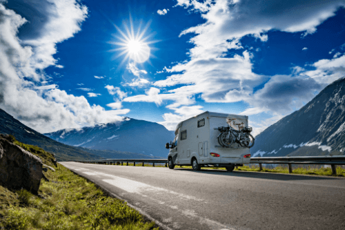 How To Prevent Tire Blowouts During Your Summer RV Trip with RV Masters in Kenner La. image of rv traveling on road with blue sunny sky and mountains on each side with bikes on back bike rack