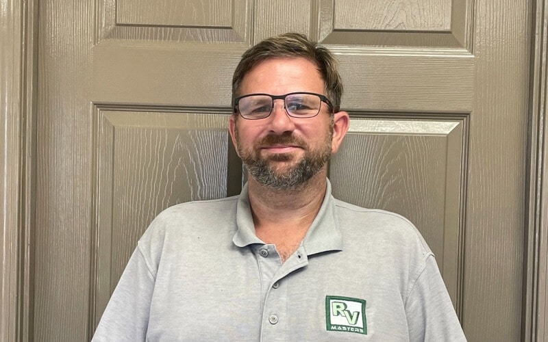 RV Masters Team president and owner, Tim Switzer in RV Masters gray uniform shirt standing in front of a tan door with his reading glasses on