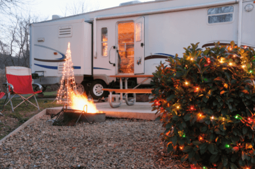 5 Tips for Surviving the Holidays as a Full-Time RVer in New Orleans, La with RV Masters in Kenner, La. image of parked white rv with chair next to campfire and bush with christmas lights