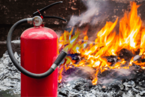 RV Fire Safety Tips For Your Kenner, LA Camper | RV Masters. Image of red fire extinguisher and a fire in the background.