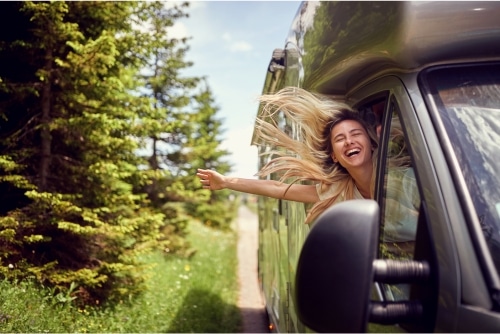 How to handle trailer blowout damage on your RV with RV Masters in LaPlace, LA. Image of happy blonde woman traveling on sunny day in RV with her arm hanging out the RV window.