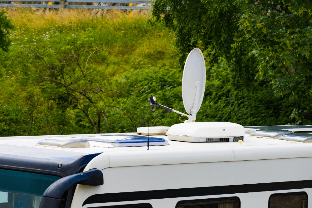 rv satellite repair, RV repair in Laplace, LA at RV Masters. RV roof with a satellite dish, air vent, and skylights, parked in a green outdoor setting.