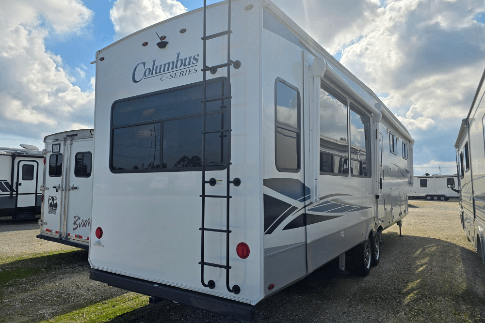 RV costs, RV repair in Laplace, LA at RV Masters. Rear and side view of a white Columbus C-Series fifth-wheel RV parked on a gravel lot under a partly cloudy sky.