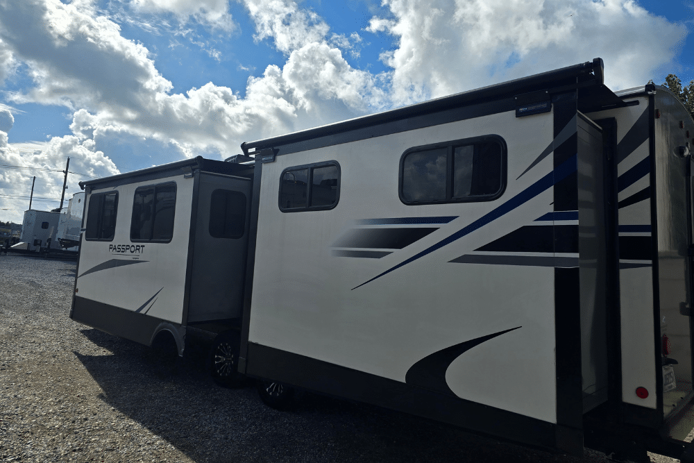 Slide-Out Roof Maintenance, RV repair in Laplace, LA at RV Masters. White Passport travel trailer with extended slide-outs parked under a partly cloudy sky at an RV lot.